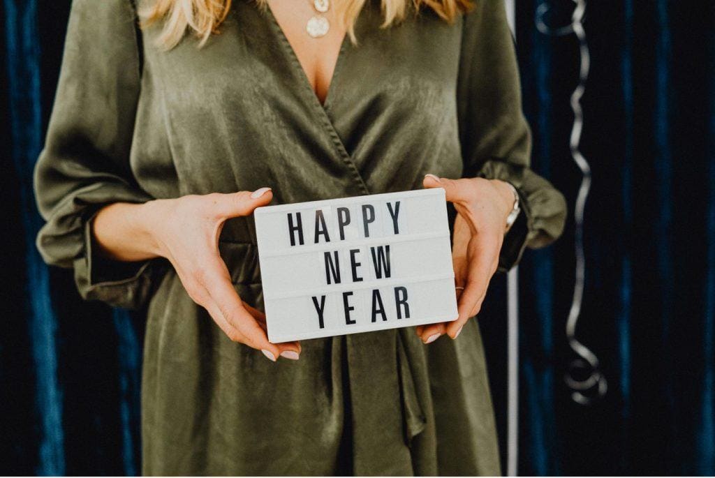 New Year's Resolutions from Tampa Counseling Place in Tampa, Florida: Person wearing an olive green silk dress holding a white lightbox sign displaying 'HAPPY NEW YEAR' against a dark blue background with silver streamers