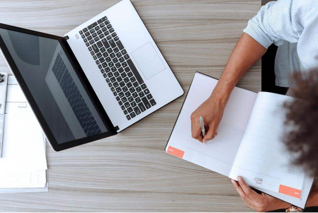 New Year's Resolutions from Tampa Counseling Place in Tampa, Florida: Overhead view of a workspace showing a laptop and someone's hands writing in a notebook on a light wooden desk surface