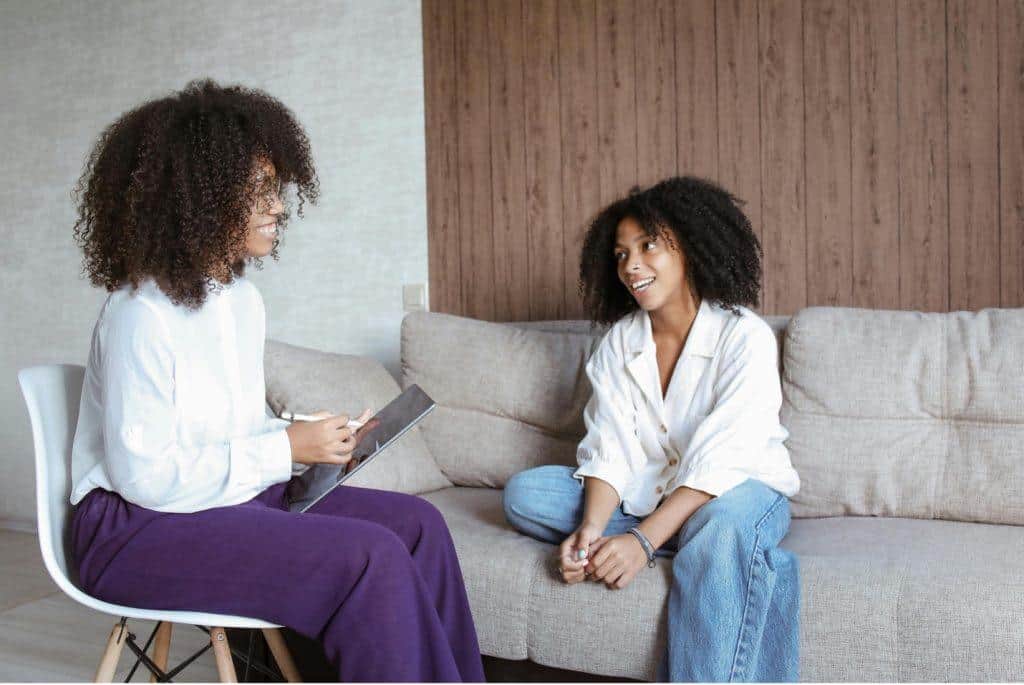 Find the right therapist in Tampa, FL. with Tampa Counseling Place. Two women sitting and talking, one holding a tablet and taking notes, suggesting a therapy or counseling session in a relaxed setting.