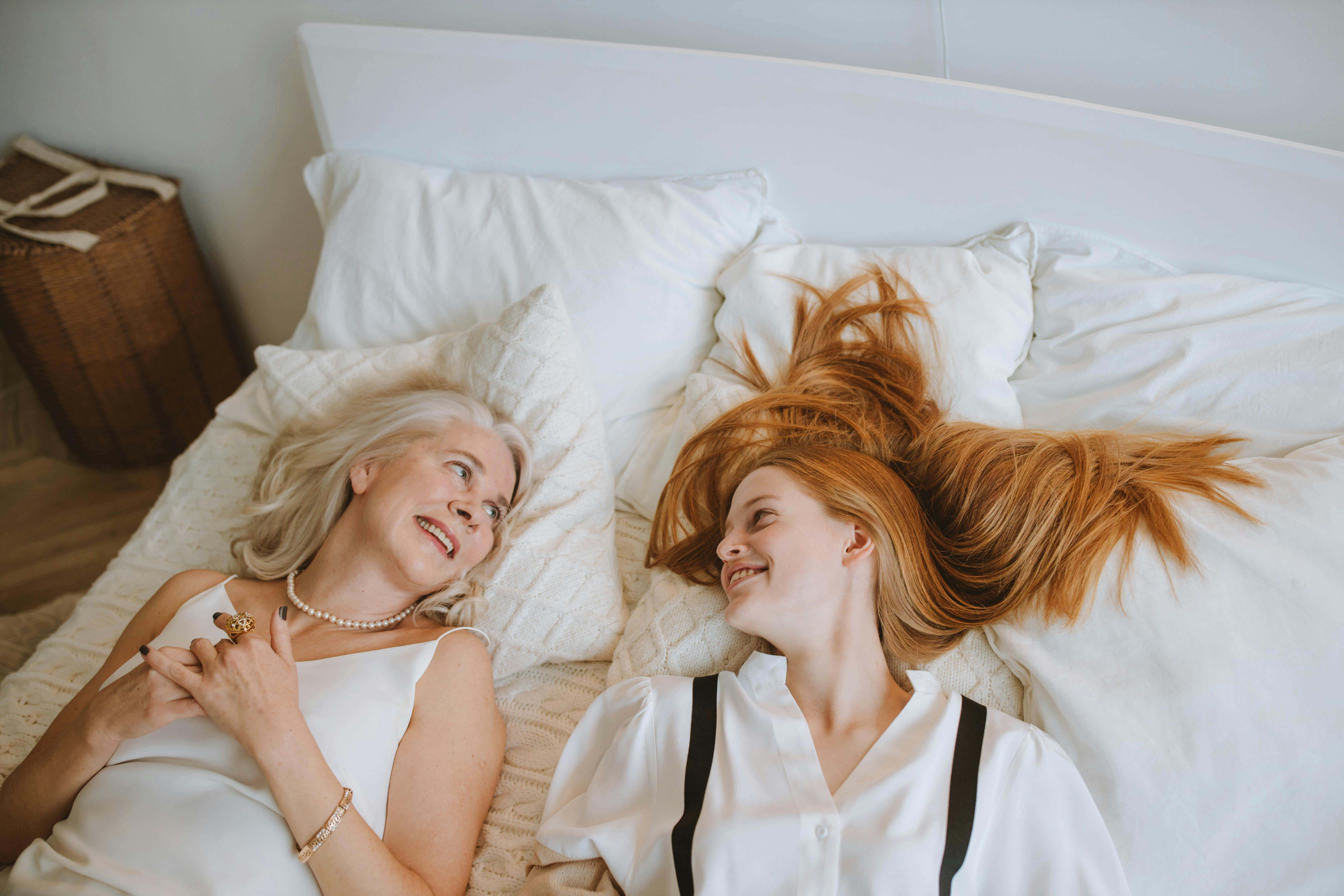 Teen therapy in Tampa, FL. at Tampa Counseling Place. The image shows two women relaxing on a bed. One has blonde hair and is smiling, the other has reddish hair that appears windblown. They seem comfortable together.