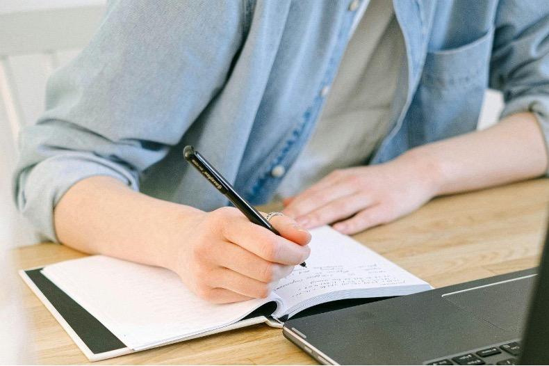 Online vs. In-Person Therapy | Which Is Right for You? Tampa Counseling Place person's chest and torso view, writing in a journal on a desk in front of a laptop