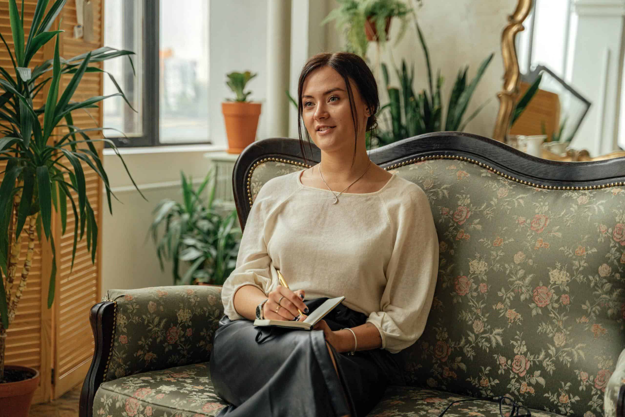 What to Expect in Your First Therapy Session - Tampa Counseling Place, woman sitting on a green floral couch taking notes looking into the distance